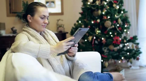 Young woman with tablet computer sitting on sofa, christmas tree in background Stock Footage 10742365