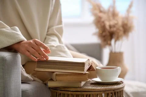 Young woman taking book from stack on table at home, closeup Stock Photos