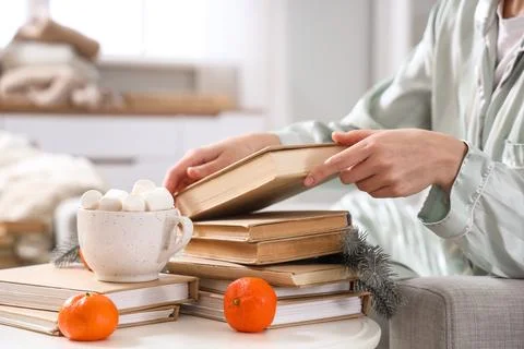 Young woman taking book from stack on table at home Stock Photos