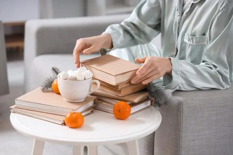 Young woman taking book from stack on table at home Stock Photos