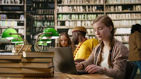 Young woman taking notes on laptop and studying beside open book Stock Footage 337229431