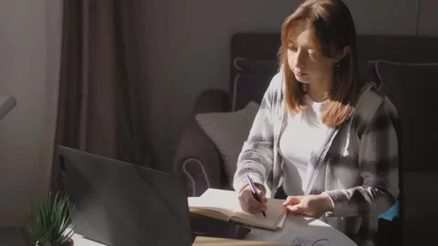 Young woman taking notes while studying on laptop at home Stock Footage 314525632