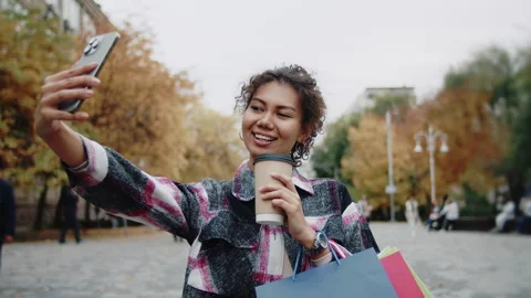 Young woman taking a selfie while holding shopping bags and coffee Stock Footage 313907500