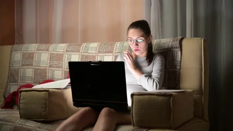 Young woman talking on the phone while working on laptop at home in the evening Stock Footage 145177261