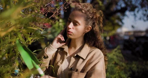 Young woman talking on phone while pruning plants in a sunny garden center Stock Footage 338369045