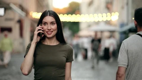 Young woman talking on smartphone while walking through city street in the Stock Footage 320362242
