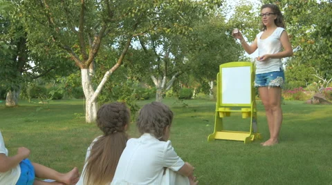 Young woman teaches the children in the garden Stock Footage