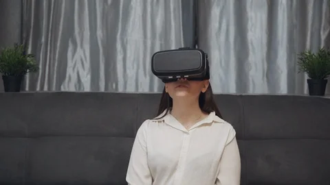 Young woman testing virtual reality glasses while sitting on sofa in home Video stock 123500259