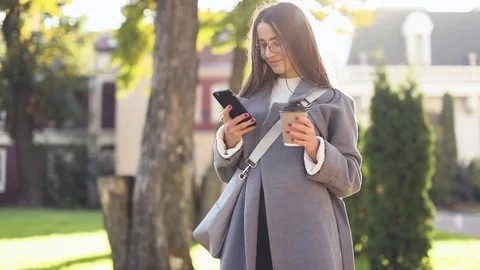 Young woman texting or using smartphone and drinking coffee in the street Stock Footage 122029845