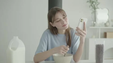 Young woman texting as she eats her chocolate cereal Stock Footage 263701748