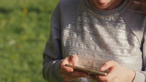 Young woman texting using smartphone on background of a blooming apple-tree at Stock Footage 136664589