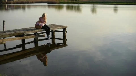 Young woman throwing flower while sitting on a pier by the lake on a sunny .. Stock-Footage 74103318