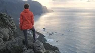 Young Woman On Top Of A Mountain Near Cliff Edge Above The Ocean Observes Sunset Stock Footage