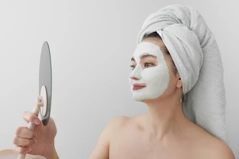 A young woman with a towel on her head and a cosmetic mask on her face smiling Stock Photos