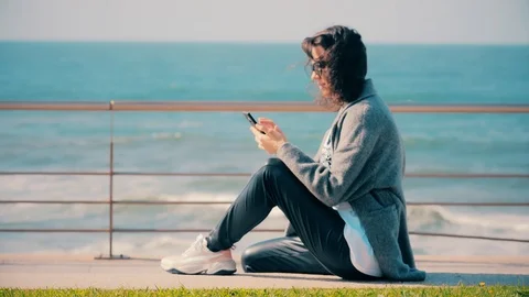 Young woman typing chat message on cell phone on beach. Brunette girl reading or Vídeos de archivo 123830896