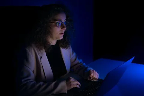 Young woman typing on computer while it is night time. Blue lights. Stock Photos