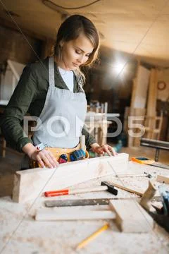 Young woman in uniform of carpenter looking at wooden plank Stock Photos
