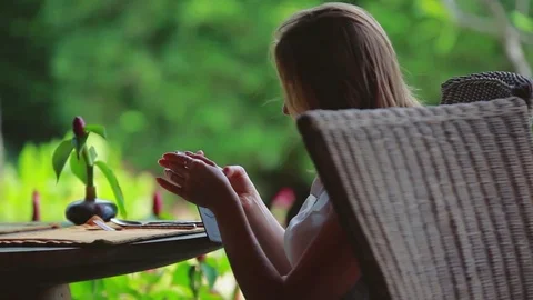Young woman uses mobile phone in outdoor cafe on blurred nature background Stock Footage