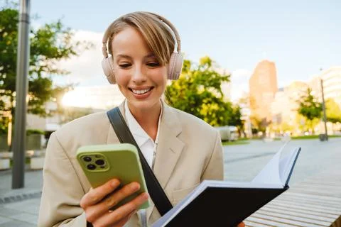 Young woman using cellphone and note book while walking on city street Stock Photos