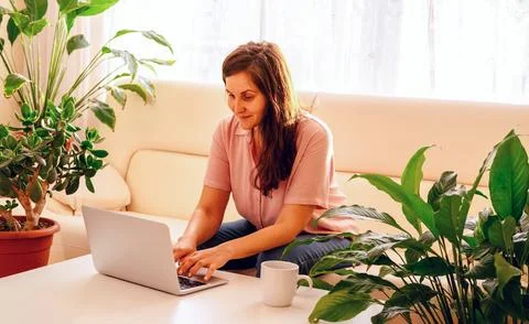 Young woman using computer in her apartments with a lot of green plants. 스톡 사진