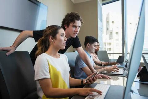 Young woman using computer in office typing on keyboard and checking mobile Foto stock