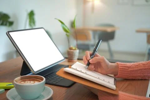 Young woman using computer tablet and making notes on her notebook. Stock Photos