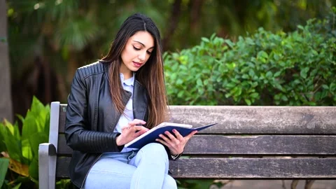 Young woman using a digital tablet sitting on a banch in a park Stock Footage 243123713