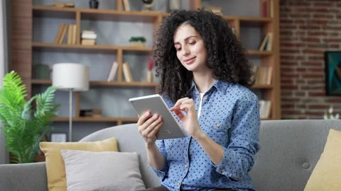 Young woman using digital tablet sitting on sofa in living room at home. Video stock 320415481
