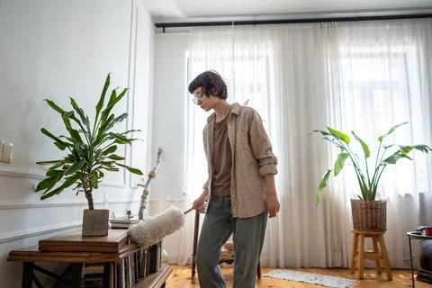 Young woman using duster to remove dust from furniture in apartment during home Stock Photos