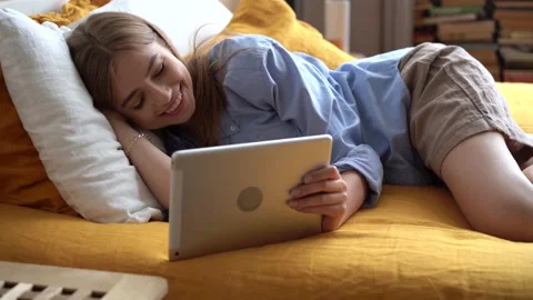 Young woman using gadget, talking on tablet lying on bed indoors Stock Footage 138931784