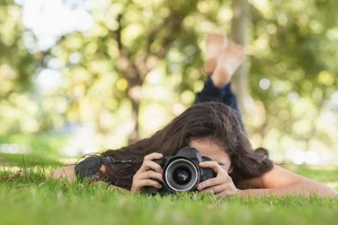 Young woman using her camera for taking a picture lying on a lawn 스톡 사진