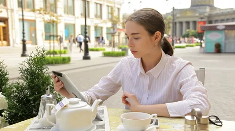 Young Woman Using Her Digital Tablet and Talking on a Phone At A Sidewalk Cafe Stock Footage 53200022