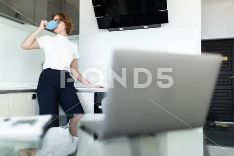 Young woman using her laptop and having a tea in her kitchen Stock Photos