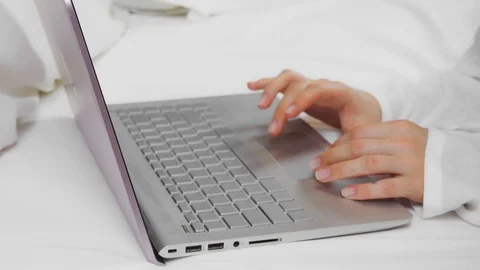 Young woman using a laptop computer while sitting on her bed at home. Vídeos de archivo 124260063