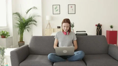 Young woman using laptop computer sitting on sofa at home Stock Footage 192377475
