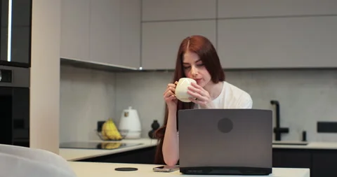 Young woman using laptop computer at kitchen. Female using a computer to browse Stock Footage 269217684