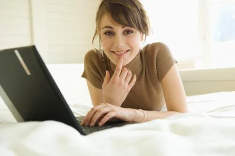 Young woman using laptop computer, lying on bed, looking at the camera Foto stock