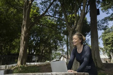 Young woman using a laptop at day time with a green park in the background. H Stock Photos