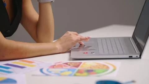 Young woman using laptop touchpad while reviewing colorful nutrition charts and Stock Footage 343922766