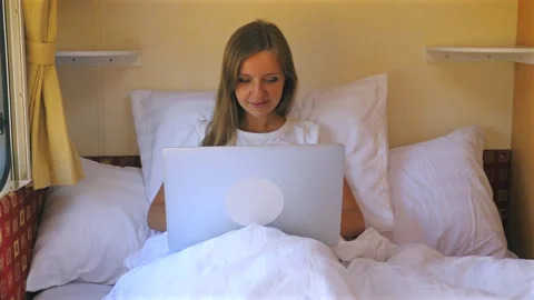 Young woman using laptop while relaxing in bed inside cozy RV during Stock Footage 287941460