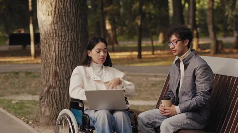 Young woman using laptop while talking to man sitting on bench Stock Footage 291864976