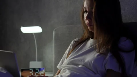 Young woman using laptop while lying in bed at night. Woman working late on.. 스톡 동영상 295285025