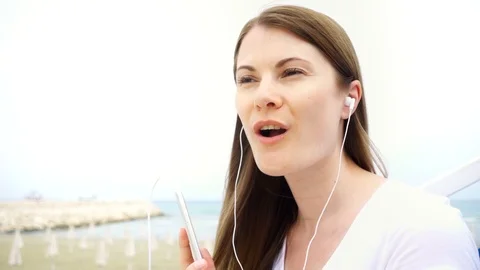 Young woman using mobile on beach alone. Female listen music via cellphone and Stock Footage 89587918