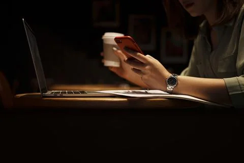 Young woman using mobile phone and holding coffee papercup while sitting at cafe Stock Photos