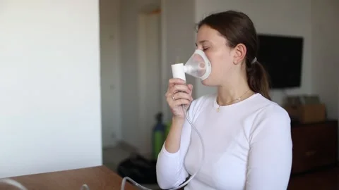 Young woman using a nebulizer mask to manage breathing Video stock 320559341