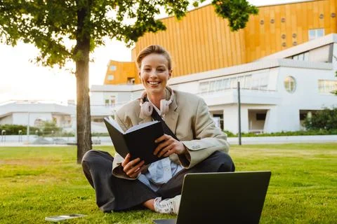 Young woman using note book and laptop while sitting on grass outdoors Stock Photos