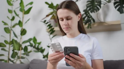 Young woman using phone for reading,  pills label text about medical information Stock Footage 251118667
