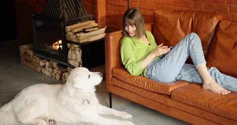 Young woman using phone while sitting relaxed with her cute white dog on a couch Stock Footage 201510587