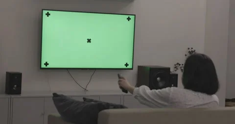 Young woman using the remote control for watching TV on green screen Stock Footage 142919747
