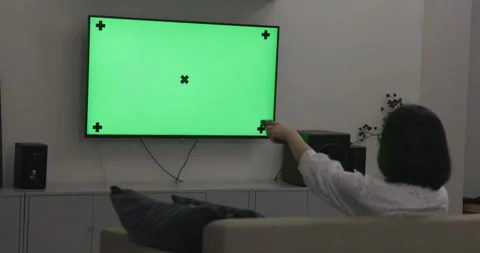Young woman using the remote control for watching TV on green screen Video stock 144250873